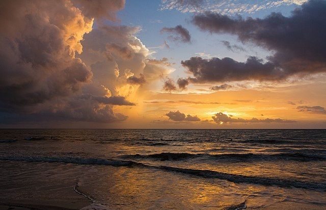 Colour photo of a sunrise over water. This image is on Wikimedia Commons, with the following title: "Sunrise_surfing,_pre-Erika_(20789490989)". If you have taken the time to access this text, may today be nothing but kind to you and yours.