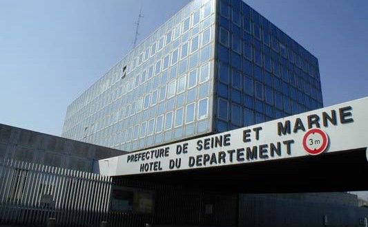 Photo d’un grand bâtiment. On voit notamment un cube couleur bleu-vert avec des fenêtres alignées comme sur le carton du post de départ. Sur la gauche, une grille et un bout de bâtiment. Sur la droite, on voit une avancée. Il est écrit préfecture de Seine-et-Marne, hôtel du département. Le tout semble sortir tout droit des années 1960.