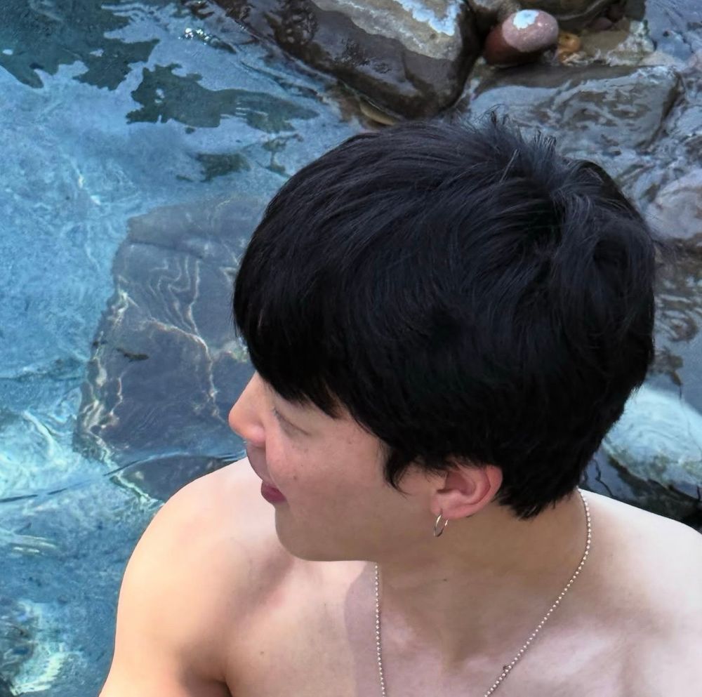 Jimin at a pool, or like the ocean or something, I'm not sure what the ocean looks like I'm from the Midwest sorry.
Anyway he's shirtless and looking to the side. You can see his freckly face and he looks happy. 