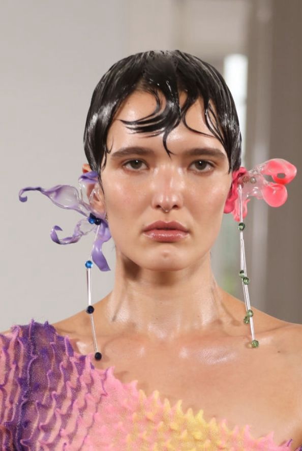 Model wearing large purple flower earring and a large coral flower earring