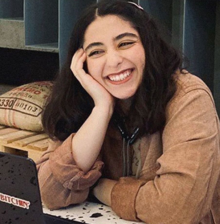 Photo de Parnia Abbassi. Elle a les cheveux mi-longs et bruns foncés, elle est assise devant un ordinateur portable et souris de manière radieuse, en regardant sur le côté, la tête posée sur sa main.