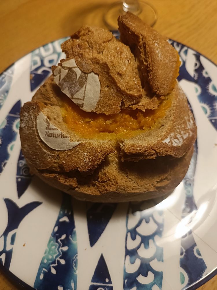 Kürbissuppe in Brotlaib auf einem griechischen Teller mit blauen Fischen