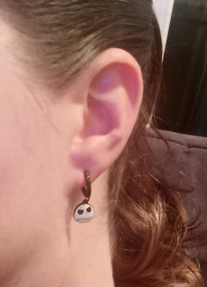 Bild meines Ohres mit einem schwarzen Ohrring, an dem das weiße Gesicht von Jack Skeleton aus "Nightmare before Christmas" hängt. Meine Haare sind in einem Pferdeschwanz zusammengefasst und hängen gewellt hinter dem Ohr 