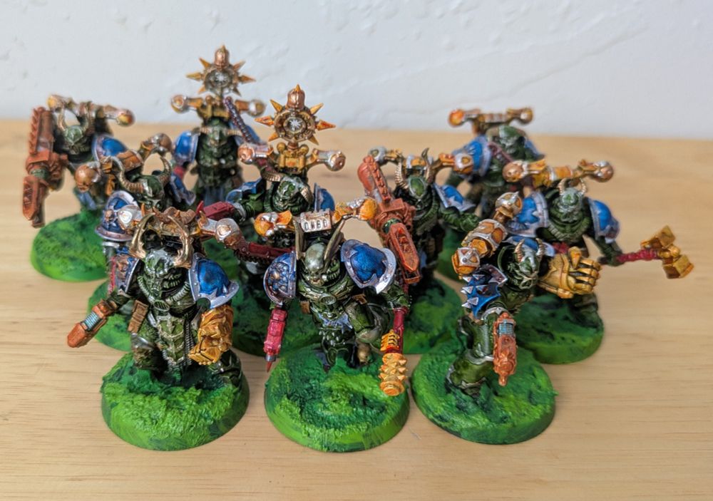 2 squads of 5 chaos space marines, mixed together for a group photo. Their armor is green, with blue shoulder pads and yellow backpacks. All the trim is platinum and bronze. Their weapons are mostly red, yellow, and orange.
