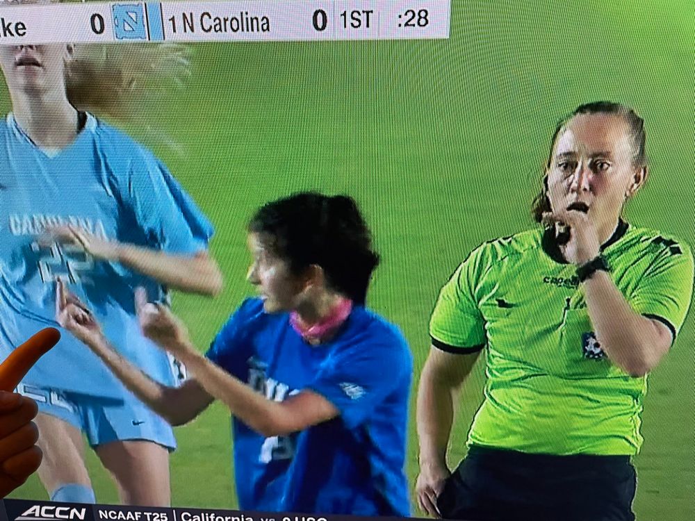 Duke women's soccer's Maggie Graham giving double birds directly in front of a ref who is already starting to blow her whistle, in a game against UNC
