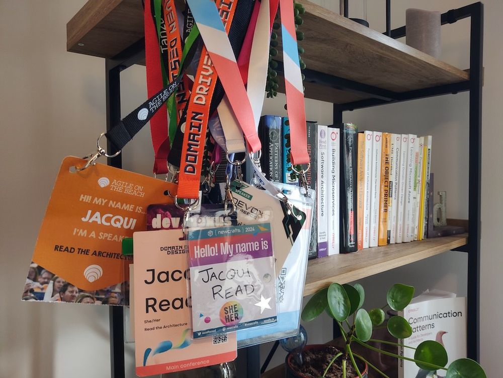 a collection of lanyards from conferences hangs on the end of some bookshelves, with a plant and software books visible in the background.