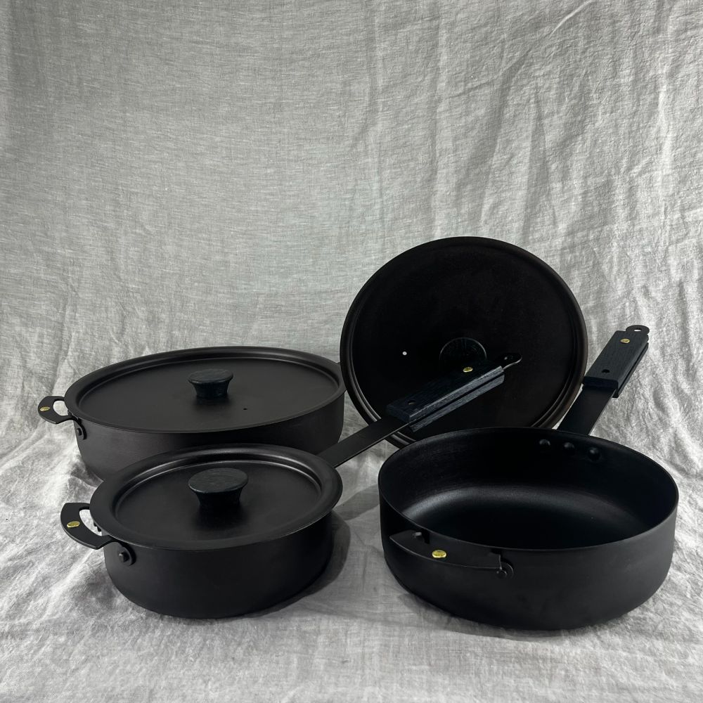 A collection of three Netherton Foundry eBonised sauteuse pans of different sized on a beige linen backcloth
