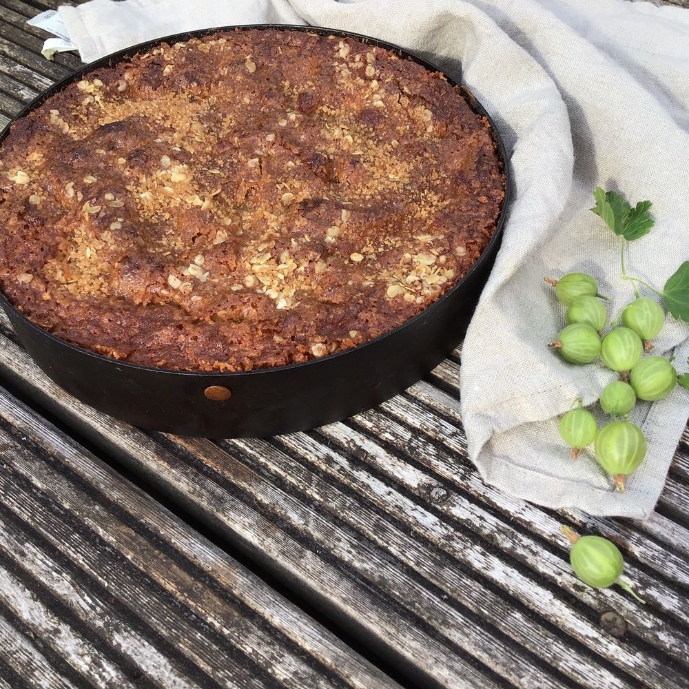 A gooseberry and oat cake (recipe from mark Diacono's book, SOUR) on a wooden table with a linen napkin and a handful of raw gooseberries