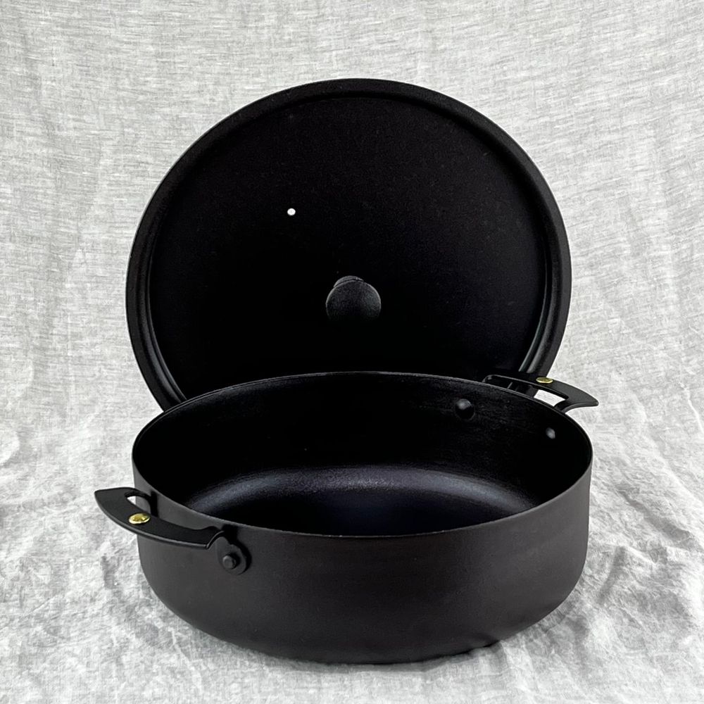 A Netherton Foundry 9 inch sauteuse prospector pan on a linen cloth, with the matching lid propped up behind