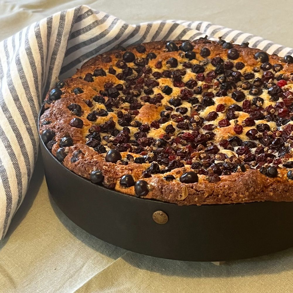 A blackcurrant cake in a Netherton Foundry cake tin, next to a grey and white striped linen napkin