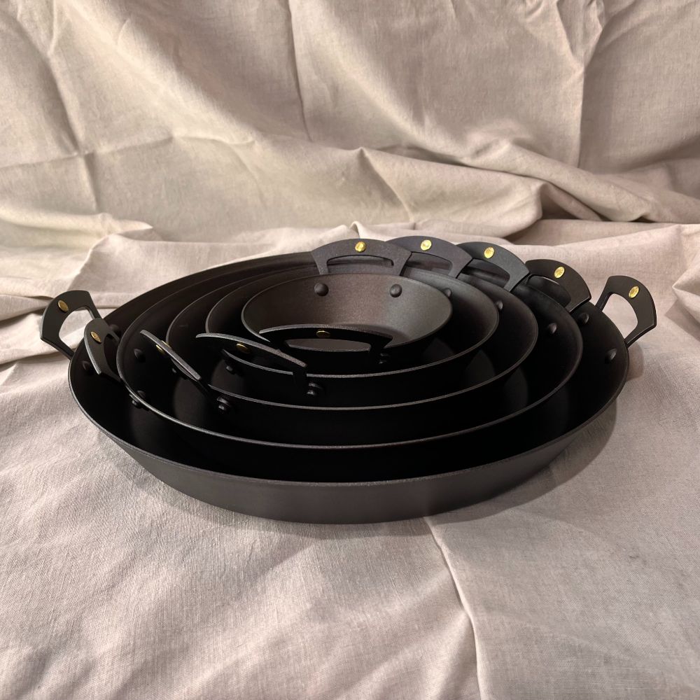 A stack of varying sized Netherton Foundry prospector pans on a linen background