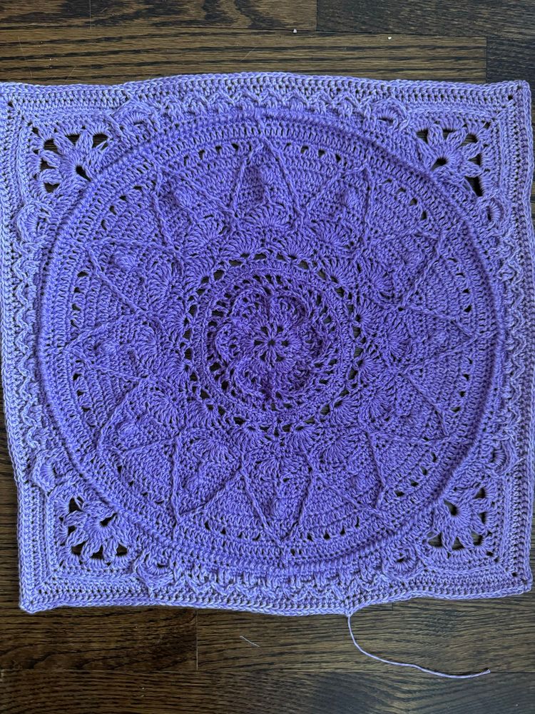 An elaborate crochet square with a mandala pattern. Worked in a fingering-weight wool/cotton blend. It’s a self-striping (self-shading?) yarn that starts as a medium purple at the centre and shades to a light purple at the edges. I haven’t measured, but the square is the same size as the first, probably about 12” across.