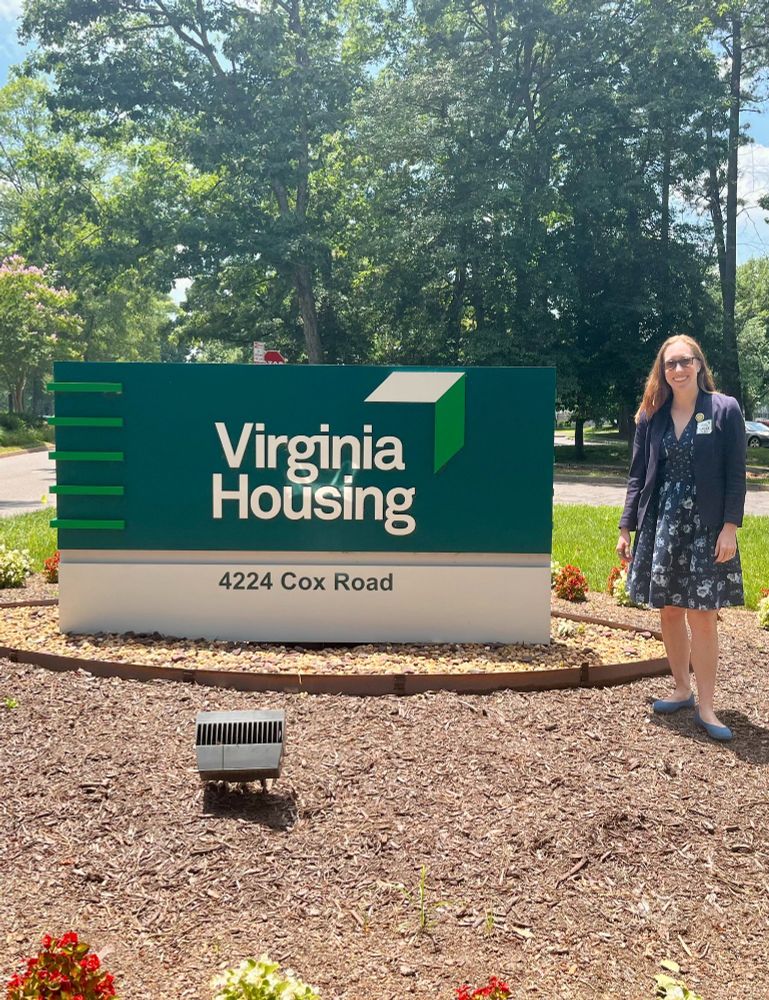 Elizabeth Bennett-Parker standing outside next to a sign reading Virginia Housing 4224 Cox Road on a hot sunny day