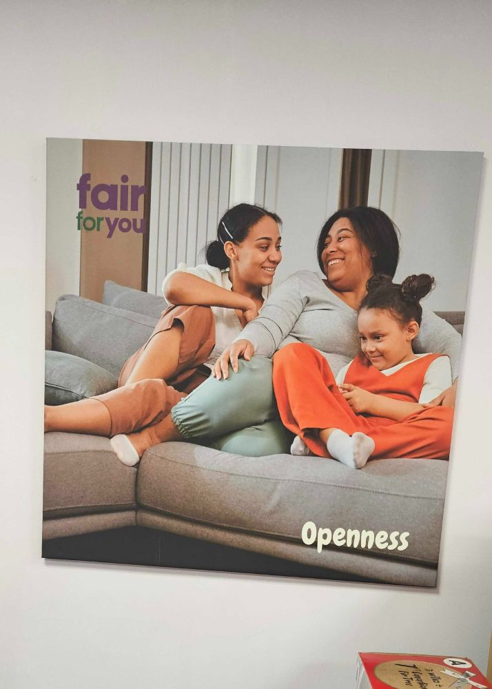 Print on office wall shows smiling family relaxing on sofa, with word 'openness' at bottom and Fair for You logo at top.