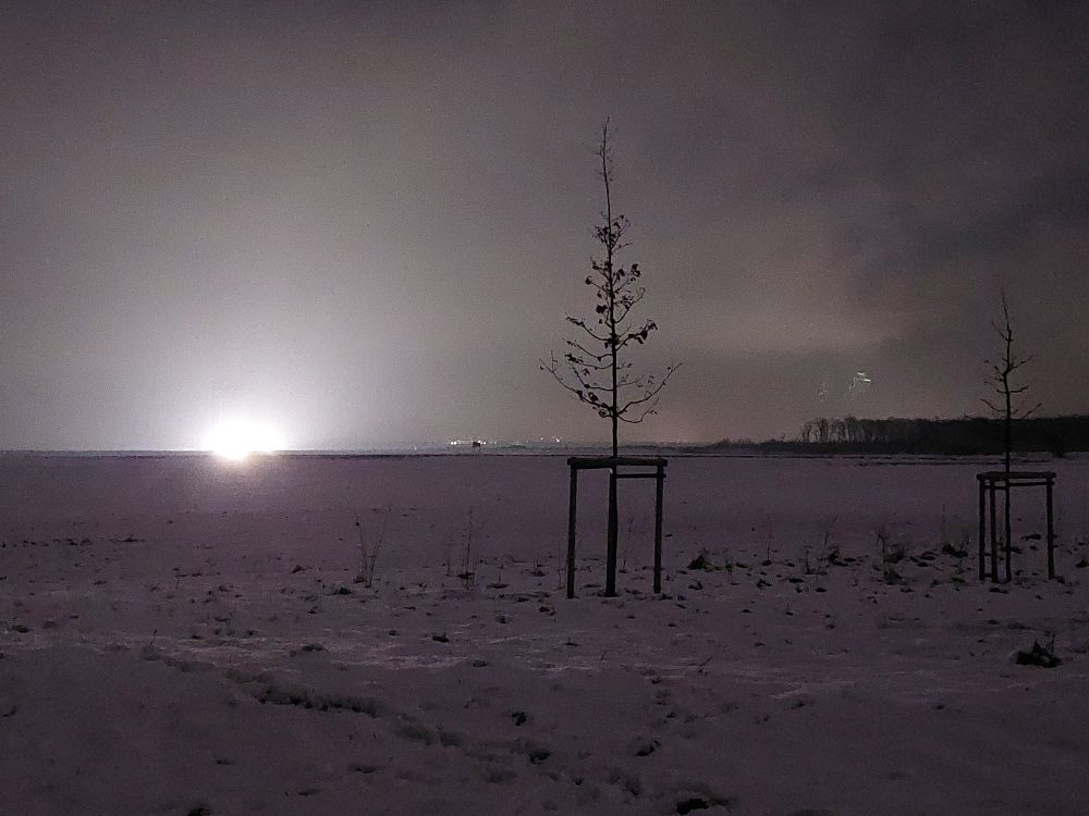 Schnee bedeckte Felder. Im Hintergrund ein Beleuchteter & arbeitender Kohlebagger 