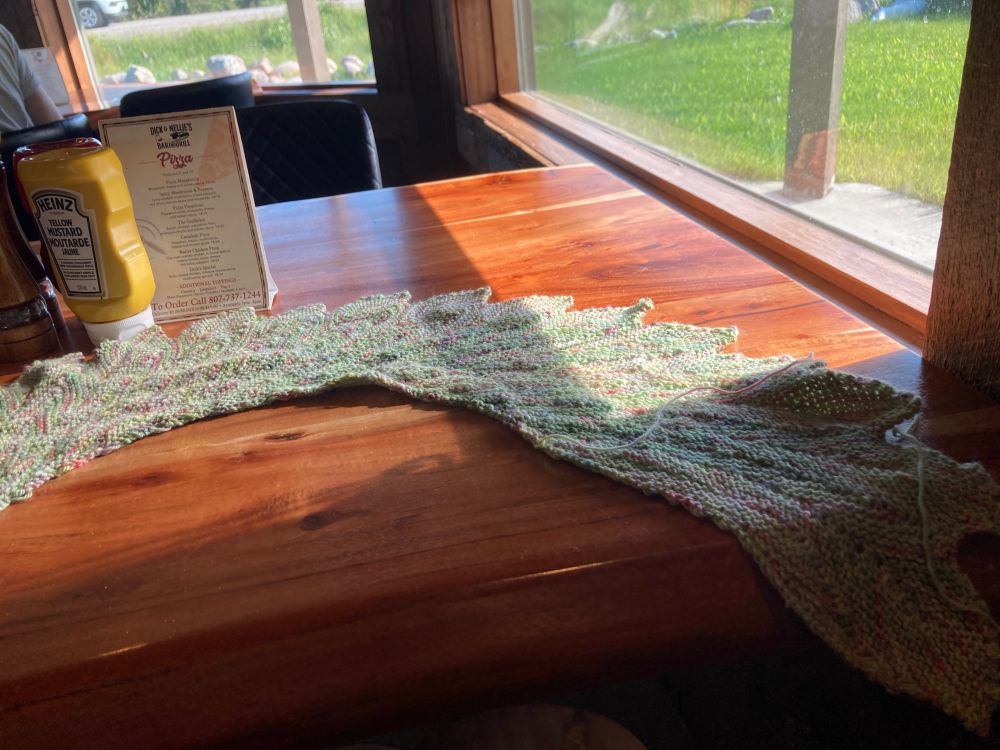 Pink and green feather shaped shawl on a wooden table. 