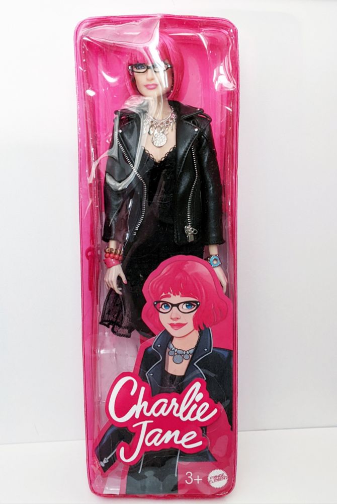 custom Barbie sized doll of author Charlie Jane Anders. The doll is a pink-haired cutie in a lace dress and wearing a leather jacket with chunky jewelry and very chic glasses. The packaging includes an illustration of Charlie Jane and the words Charlie Jane in the same typeface as the Barbie logo.
