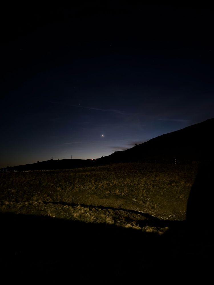 Picture of a shiny star in the evening sky, which is the planet Venus, with a mountainous landscape, right after sunset. 