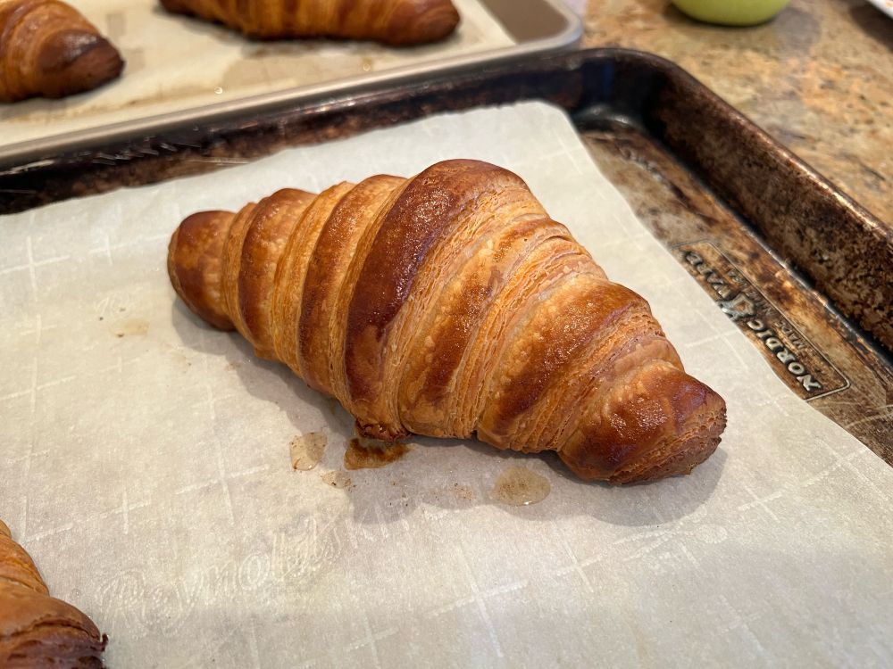 A freshly baked, homemade croissant on a parchment paper-lined baking sheet