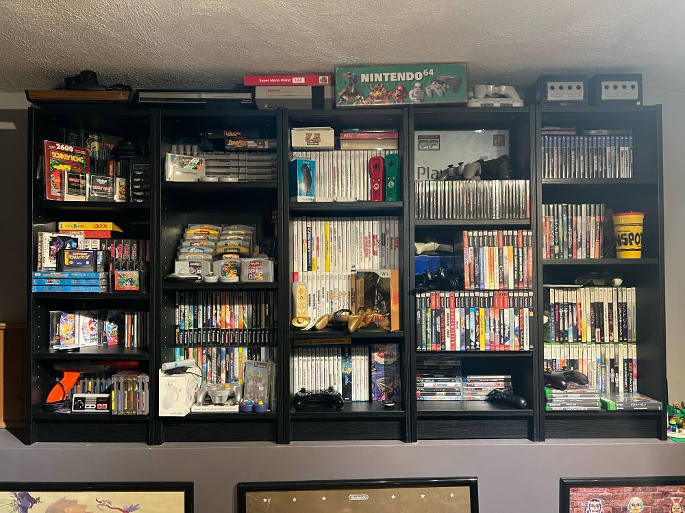 5 bookshelves filled with video games, consoles, and accessories from many generations of gaming (Atari 2600 to PS4)