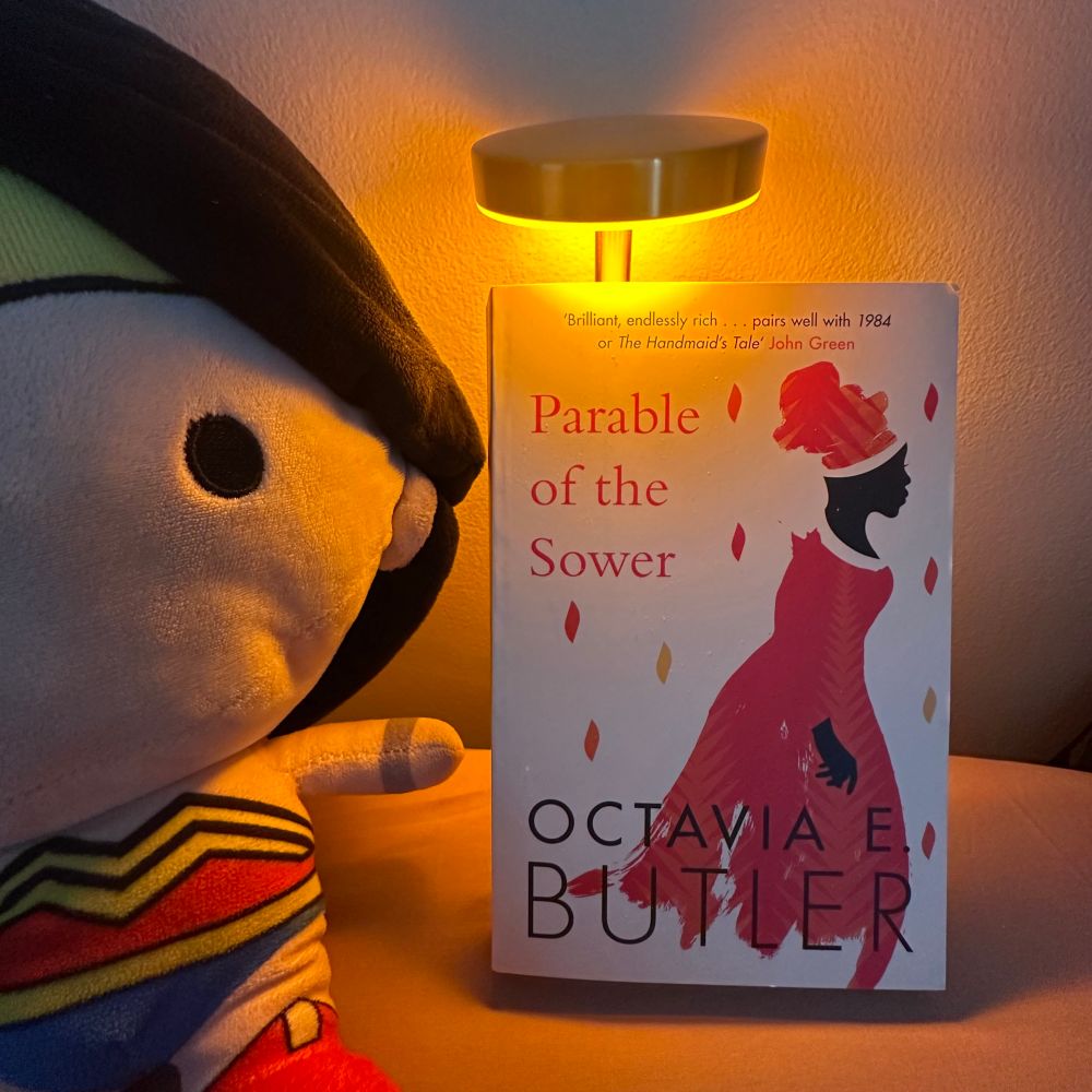 Copy of Octavia E. Butler’s Parable of the Sower under a lamp, and next to a Wonder Woman plushie. 