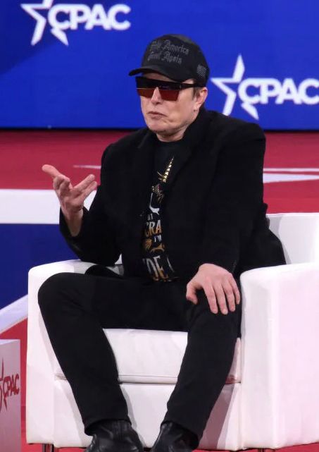 Musk in a chair wearing dark sunglasses trying to look cool.