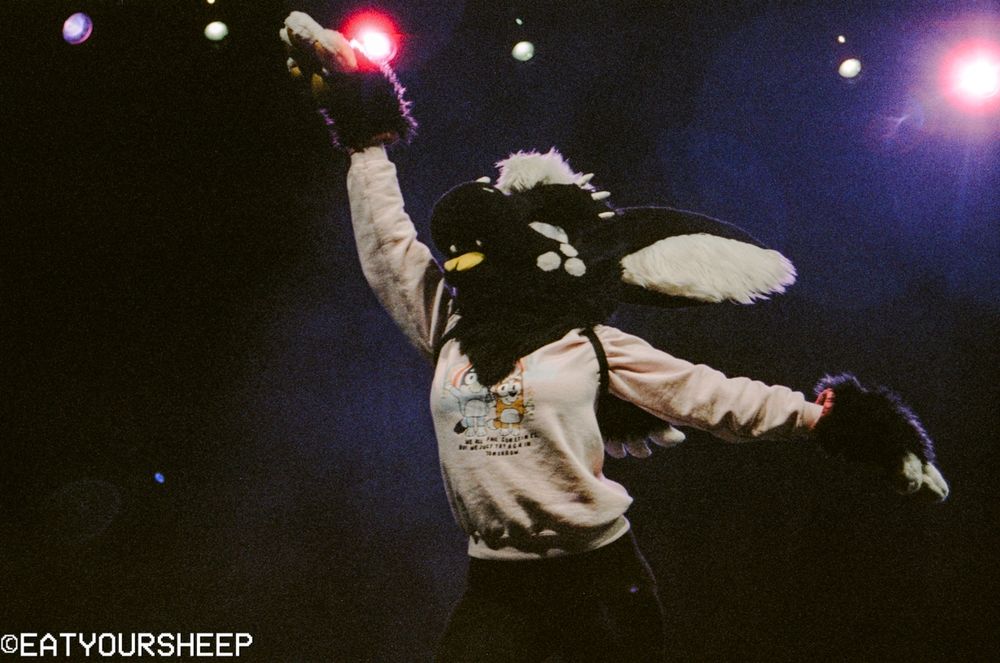 A dragon fursuiter dancing under bright lights.