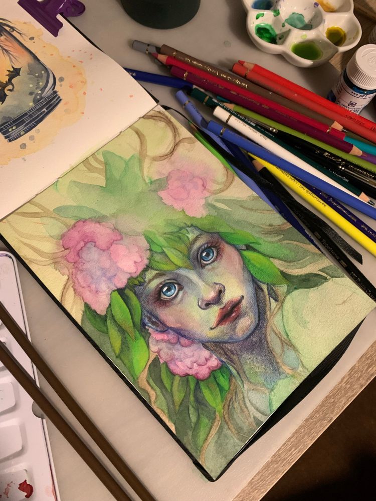 Portrait d'une femme avec une chevelure de feuilles et de fleurs. Ses yeux sont bleus. Autour, on retrouve du matériel de dessin (des pots de peintures, des crayons de couleurs et des pinceaux)