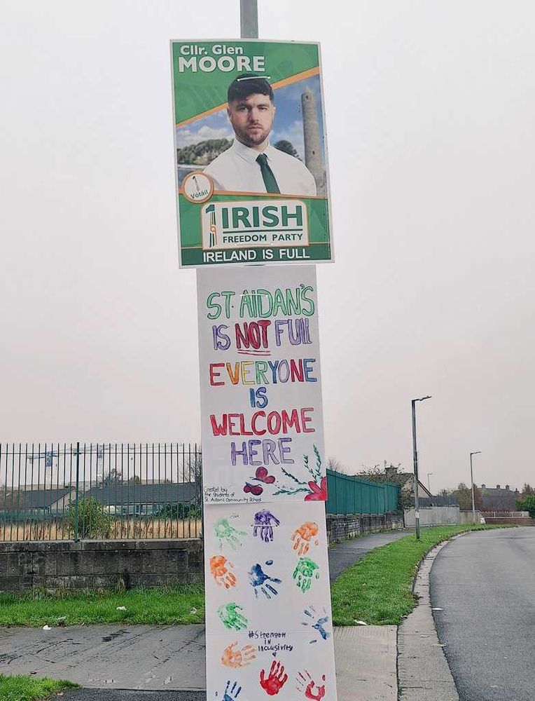 Poster of a far-right immigrant politician, claiming "ireland is full" with a hand-written poster by children under it, claiming their school is not full, and that everyone is welcome here. Some cute handprints under the poster reinforce the point.