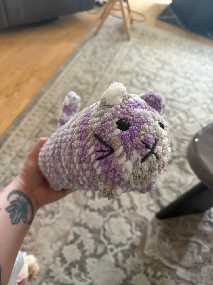 A purple and grey crocheted cat plushie.