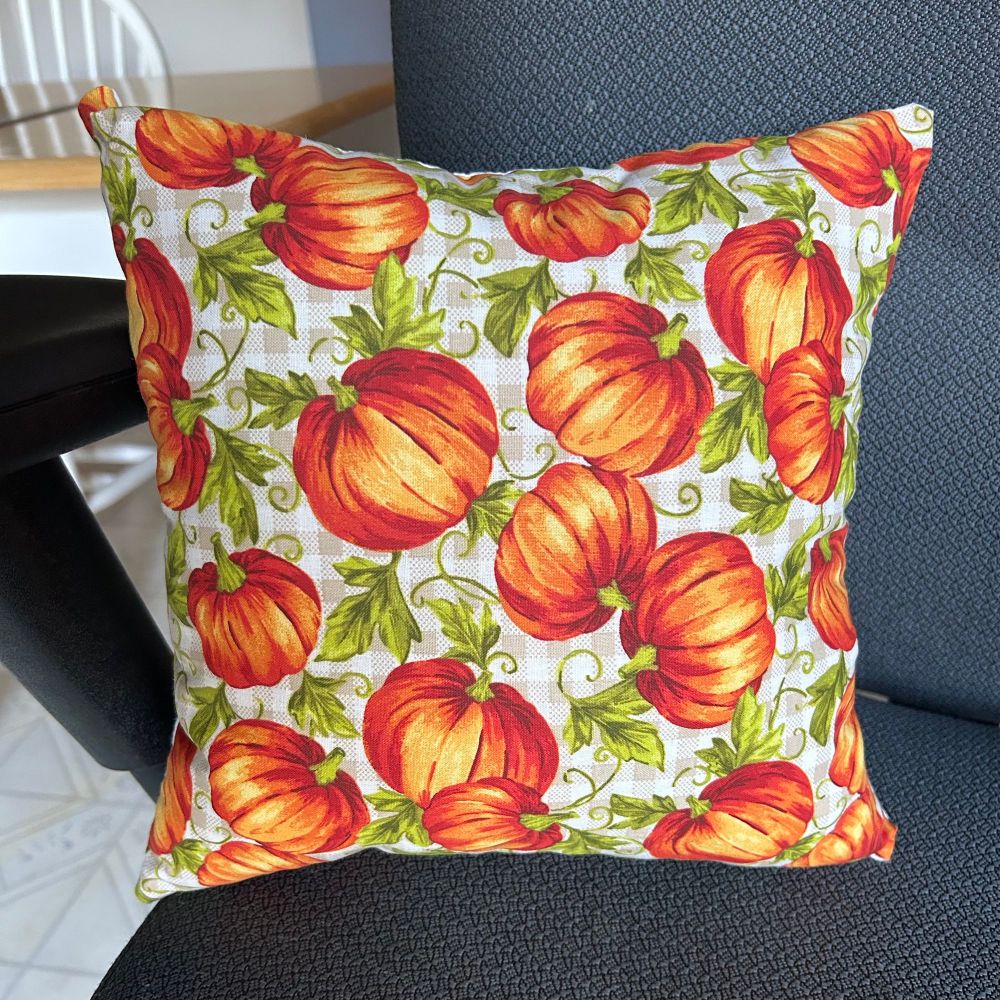 Square pillow with pumpkins and pumpkin vines printed on a tan check background