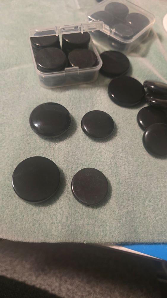 Black stone coin beads sitting on a bead mat.  Some have a defined edge and some do not