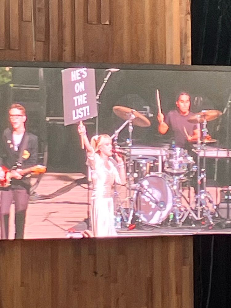 Blonde singer holding up a sign that says He’s on the list. 