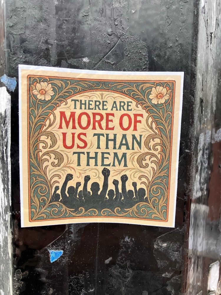 Sticker on a street light with an outline of people saying There are more of us than them 