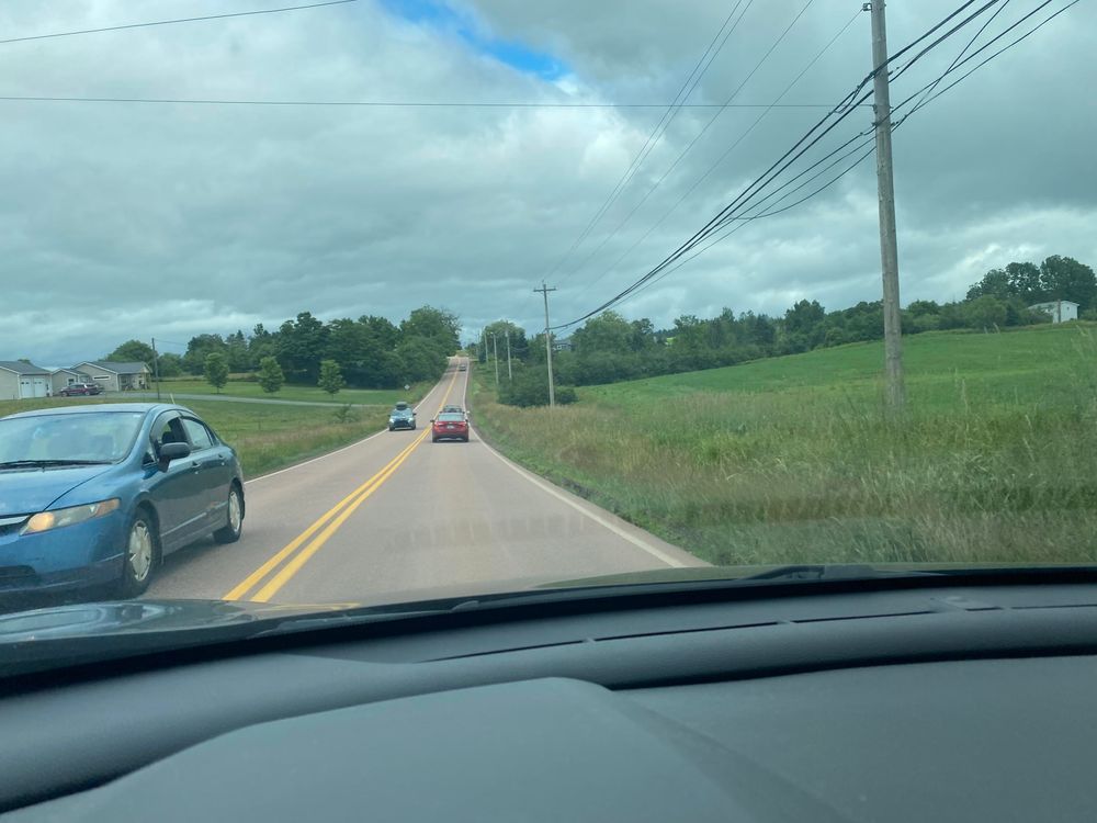 Country road with traffic, from the phone holder on the dashboard. White clouds, fields either side. 