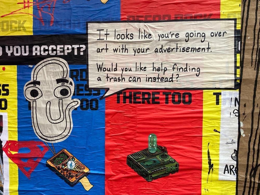 A photo of Microsoft Clippy over music advertisement flyers with the caption, “It looks like you're going over art with your advertisement. Would you like heip finding a Trash can instead?”