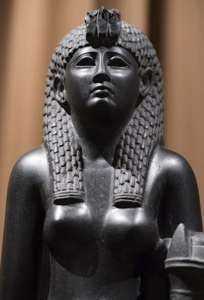 Egyptianising, 41” tall, black basalt statue of Cleopatra VII, wearing a tight ankle-length shift dress, a tripartite wig, topped by a triple uraeus and holding a double cornucopia. Held by the Hermitage Museum, St Petersburg, since 1929. 