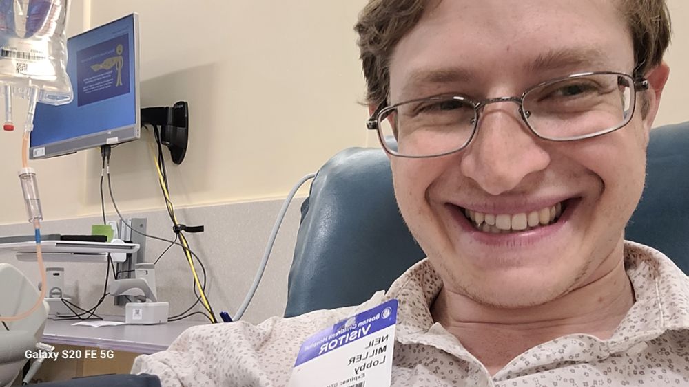 Young man with glasses smiling with IV in background 