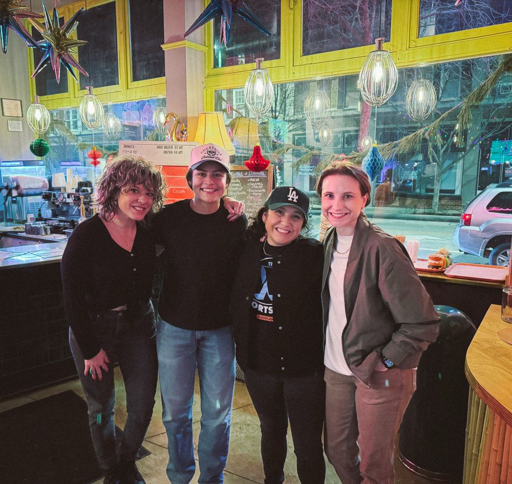 4 women standing and smiling looking at the camera 