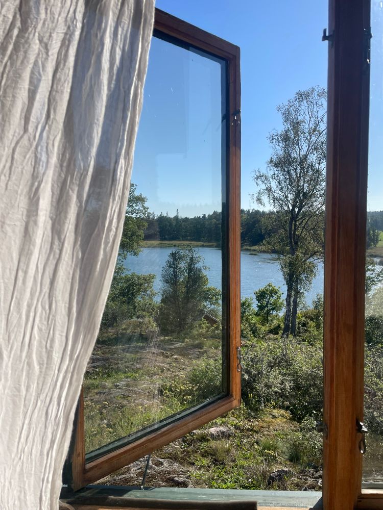Vorhang und ein geöffnetes Fenster mit dünnem Rahmen aus Holz. Natur vor dem Fenster, ein See.