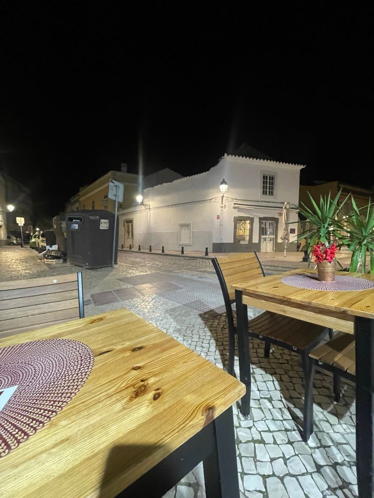 Tische und Blumen und eine Palme ganz im Dunkeln, aber es ist hell. 