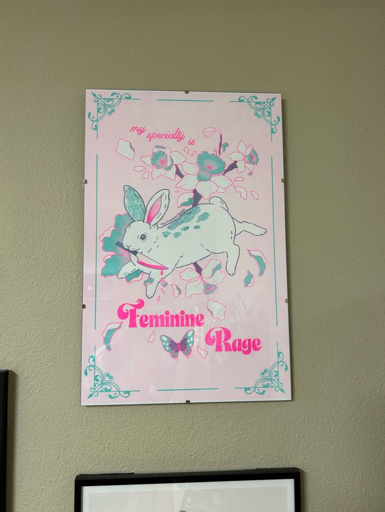 Pink, teal, and white print of a rabbit with a knife and text reading “my specialty is feminine rage” - art by @thecrownedrabbit