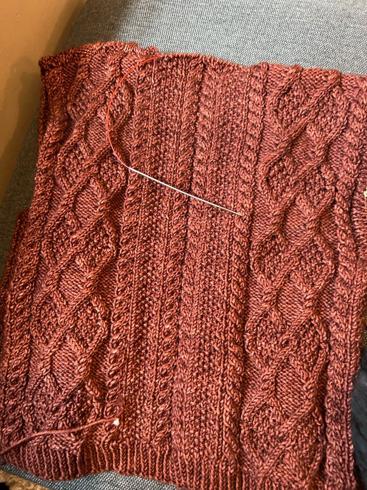 The back of a cable knit sweater in a rust-colored yarn