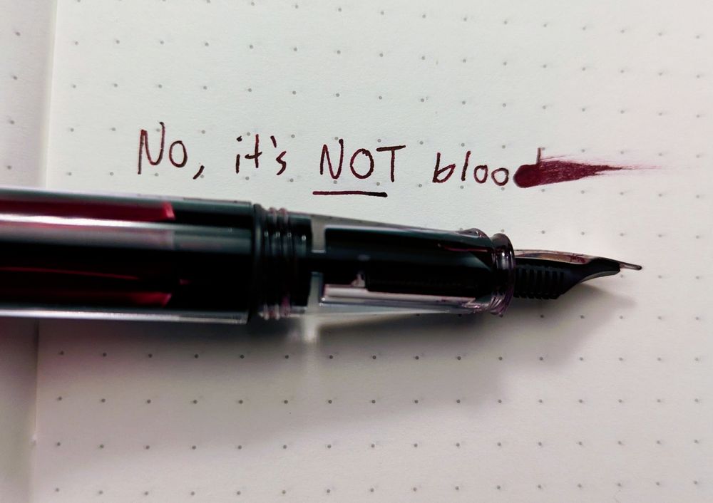"no, it's NOT blood" written in an ink that looks quite like drying blood. the "d" is smeared. 

a translucent fountain pen rests on the the paper, it's reservoir filled with a dark red ink