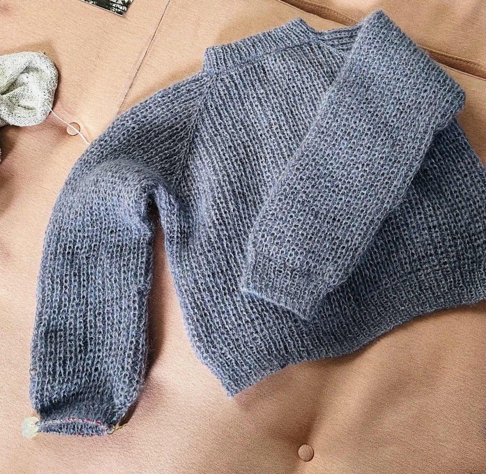 The seasons sweater designed by ozetta in a grayish lilac on a pink couch