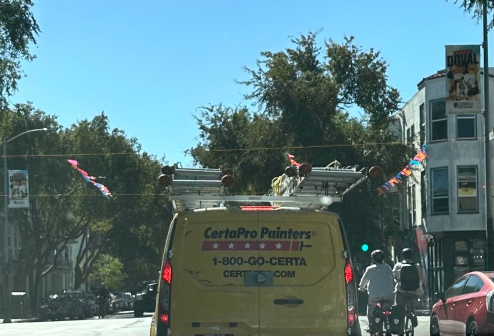 A yellow van with a precarious stack of ladders tied to the roof, from a (safely stopped) driver’s point of view