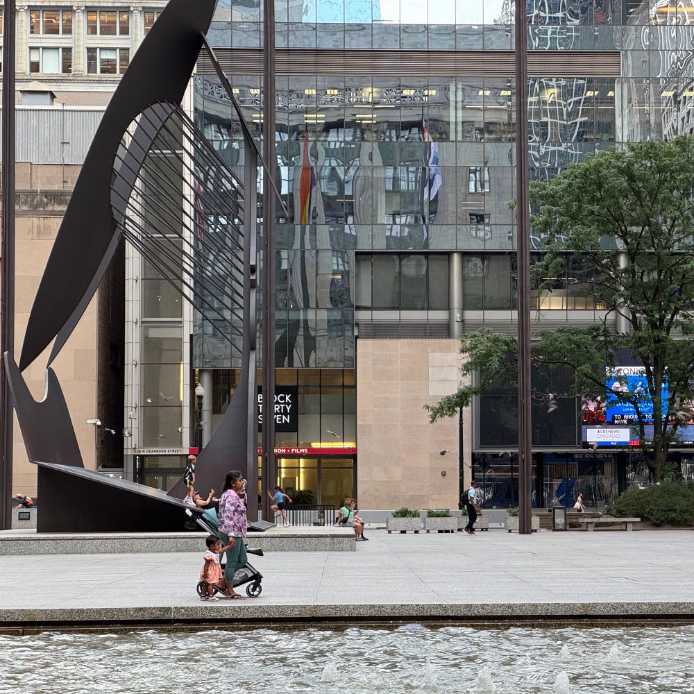a photo from the benches between the sidewalk and the fountain at daley plaza of daley plaza looking east, showing the picasso, the electrical substation behind it, and block 37.