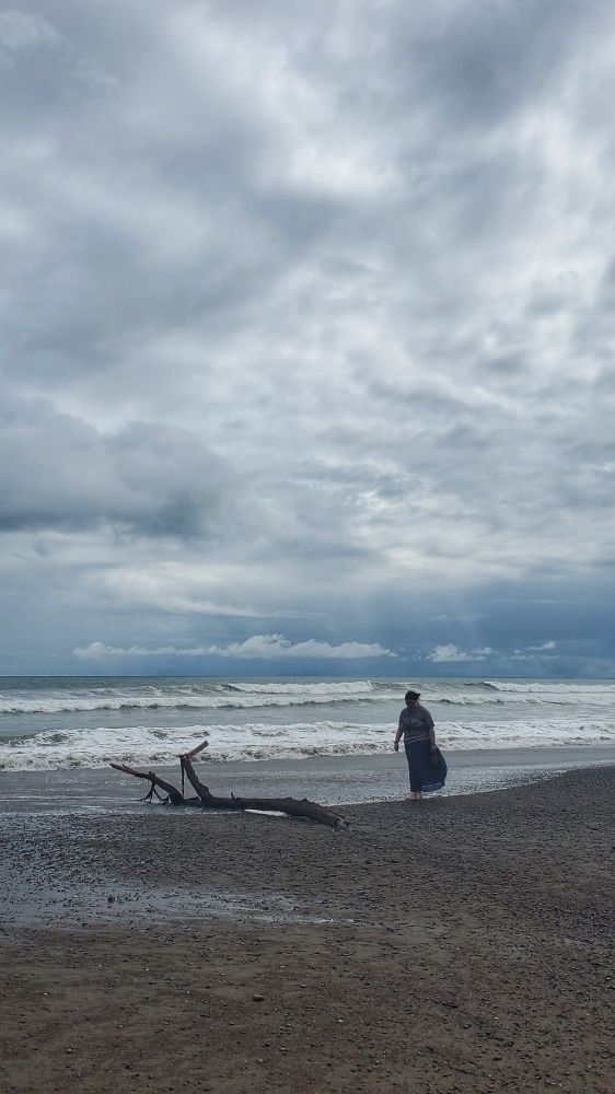 My daughter and a piece of driftwood on the beach in Costa Rica. The cloudy skies mute the beautiful colors of the Pacific Ocean. It looks like there might be rain in the distance. 