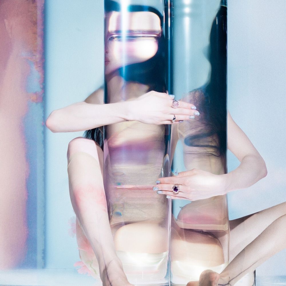 Poppy abraçando pilares transparentes que refletem partes de seu corpo 