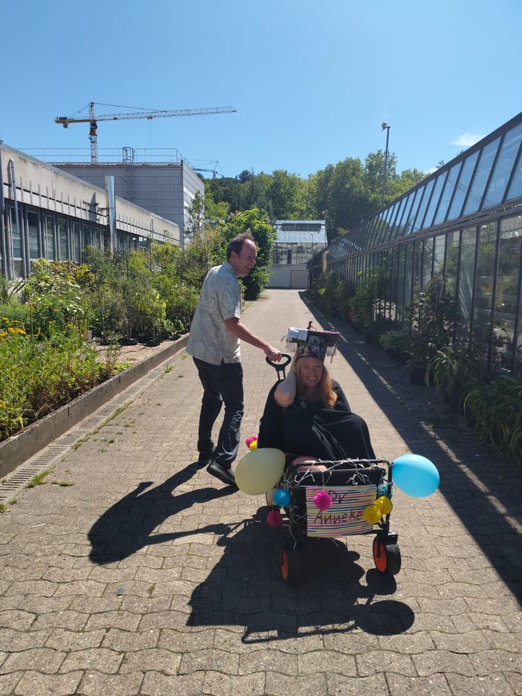Woman with graduation cap and gown sitting in a small cart being pulled by a man 